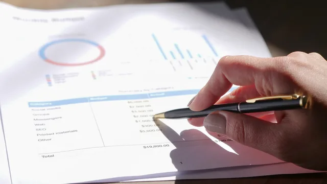Hand holding pen, analyzing budget with charts and graph paper. Selecting retail media suppliers by recording what was examined, not by scoring what was not